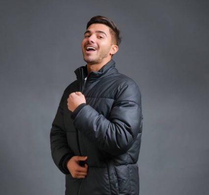 Smiling stylish guy model on a gray background is warmly dressed in a black down jacket. High quality photo